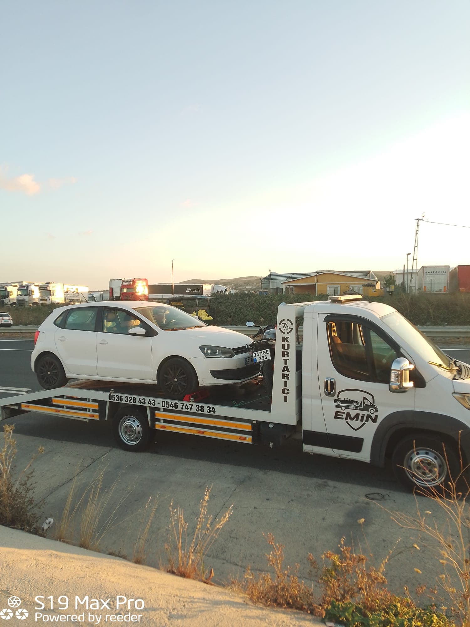 Çekici platformunda aynı anda beyaz bir hatchback ve bir motosiklet, yol kenarında gün batımında